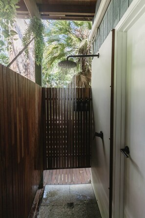 A wooden gate leading to a covered outdoor area with a shower and a door on the right.