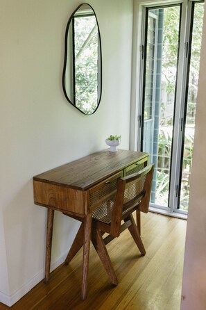 A wooden desk with a woven chair, a small plant, and a mirror on the wall.