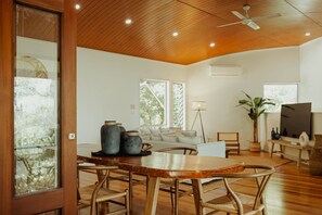A spacious living area with a wooden ceiling, a dining table with chairs, a sofa, and a television.