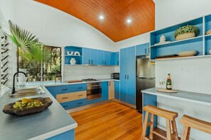 A modern kitchen with blue cabinets, a wooden ceiling, and a built-in island with a fruit bowl.