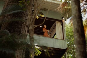 A person standing on a balcony with a view of trees and a building.