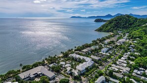 A coastal residential area with houses, a beach, and mountains in the background.