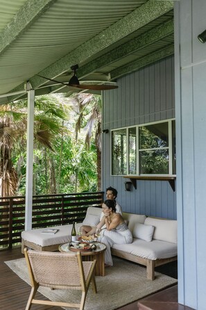 A covered outdoor seating area with a ceiling fan, a sofa, and a wicker chair.