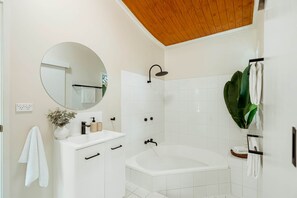 A modern bathroom with a freestanding bathtub, a round mirror, and a wooden ceiling.