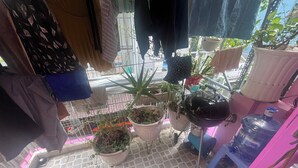 Een kleine kamer met tegels, hangende kleding, plantenpotten en een waterdispenser.