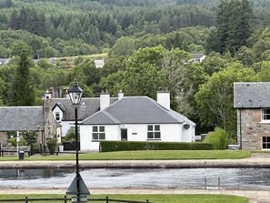 A white building with a grey roof, a lamp post, and a water body in the foreground.