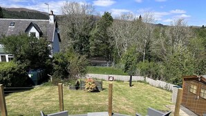 Eine Terrasse mit Gartenmöbeln, ein eingezäunter Garten und ein Haus im Hintergrund.