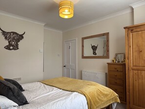 A bedroom with a bed, a wooden wardrobe, a radiator, and a wall-mounted mirror.
