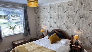 Ein Schlafzimmer mit einem Bett, zwei Nachttischen, einer Lampe, einem Fenster mit Vorhängen und einer Wand mit Muster.