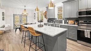 A modern kitchen with a central island, grey cabinets, stainless steel appliances, and pendant lighting.