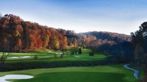 A golf course with a water hazard, trees, and a hill in the background.