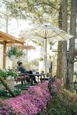 A patio area with a wooden pergola, a table with a white umbrella, and potted plants. - Dong Homestay  (Xuan Huong - Da Lat)