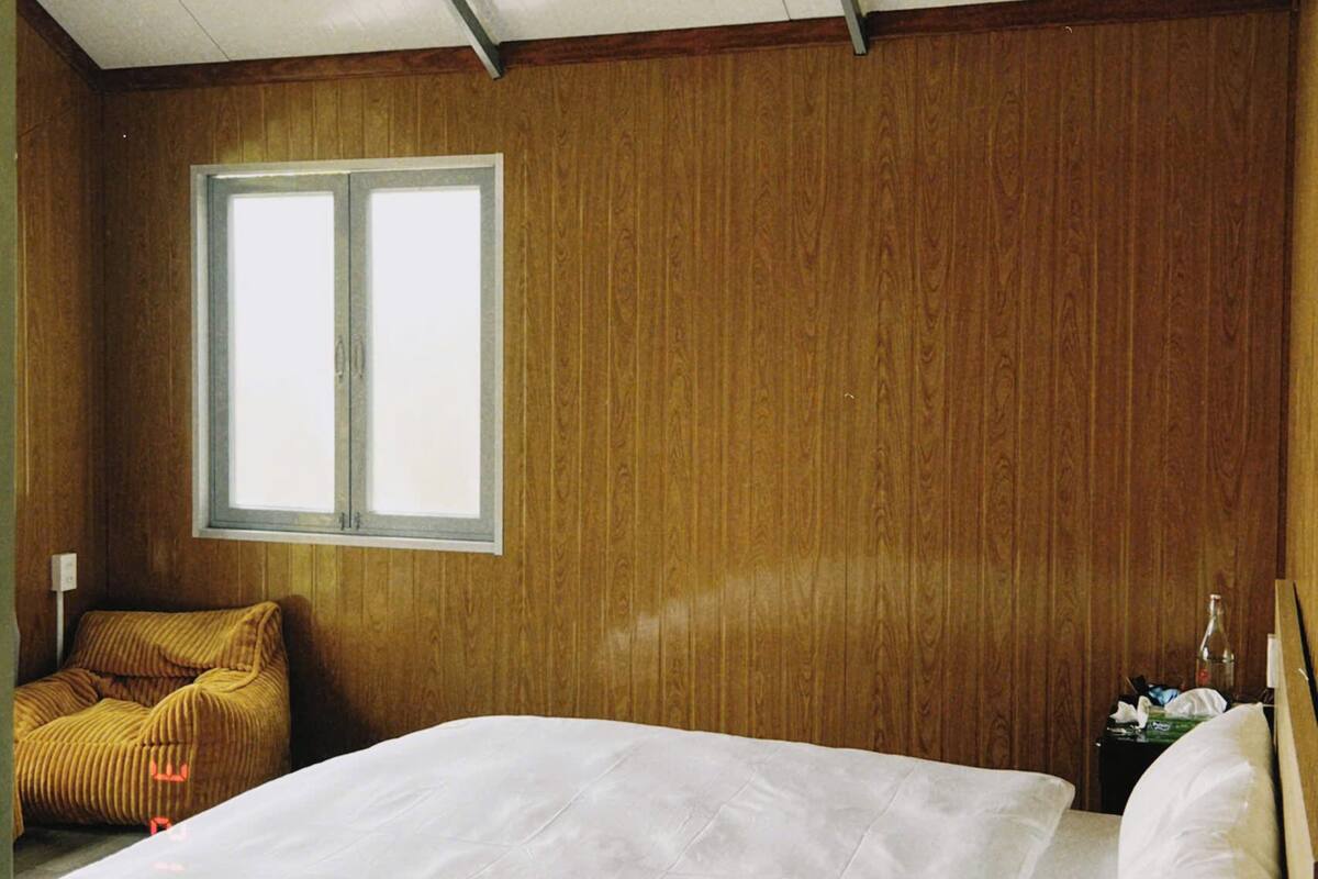 Une chambre avec un mur en bois, une fenêtre, un lit avec une literie blanche et deux luminaires circulaires au plafond.