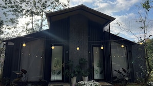 A modern building with large windows, a dark exterior, and a garden with flowers and plants. - Dong Homestay  (Xuan Huong - Da Lat)