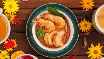 Un bol de soupe aux crevettes, entouré de fleurs et de tasses de thé, sur une table en bois.