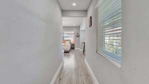 A narrow hallway with light-colored walls and wooden flooring, leading to a bedroom with a bed and a nightstand. - Walk to Beach Studio | Pompano Beach (Pompano Beach)