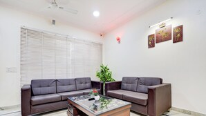 A modern living room with two dark brown sofas, a glass coffee table, and a potted plant. - Tulip Residency (Gurugram)