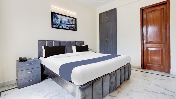 A modern bedroom with a large bed, a bedside table, a wardrobe, and a door. - Tulip Residency (Gurugram)