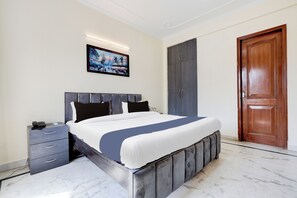 A modern bedroom with a large bed, a bedside table, a wardrobe, and a door. - Tulip Residency (Gurugram)