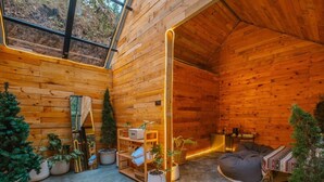 A cozy cabin interior with wooden walls, a large window, and a seating area with a sofa and bean bag. - LOUVREFER (Mae Taeng)