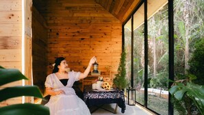 A wooden cabin interior with a large window, a table with candles, and a teddy bear. - LOUVREFER (Mae Taeng)