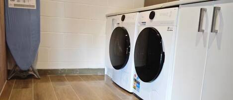 A laundry room with two front-loading washing machines, a drying rack, and a cabinet with a floral arrangement.