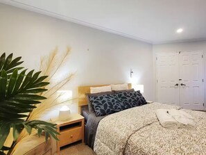 Quarto com cama, mesas de cabeceira, abajur, planta e guarda-roupa.