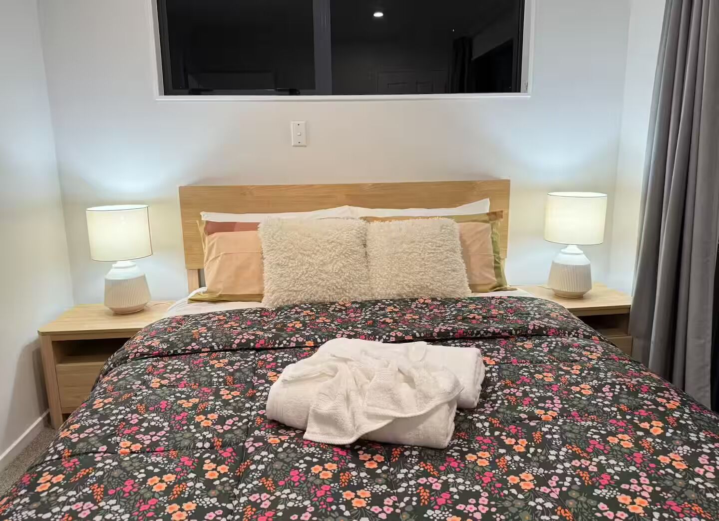 A neatly made bed with a floral bedspread, two bedside lamps, and a window above.