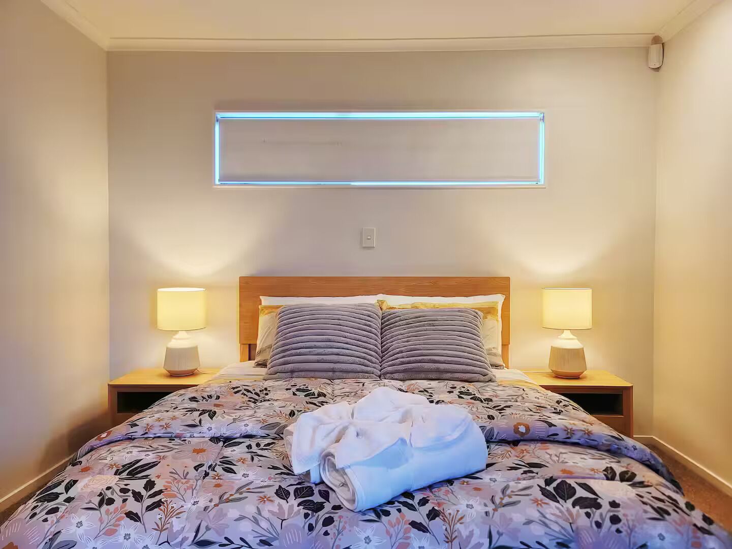 Un letto rifatto con lenzuola a motivi floreali, due abat-jour e un punto luce a parete.