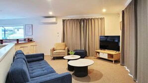 A modern living room with a sofa, two coffee tables, a TV, and a chair.