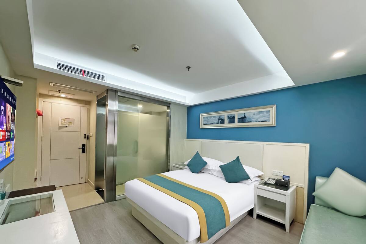 A hotel room with a bed, a nightstand, a desk, a chair, a bathroom, and a door.