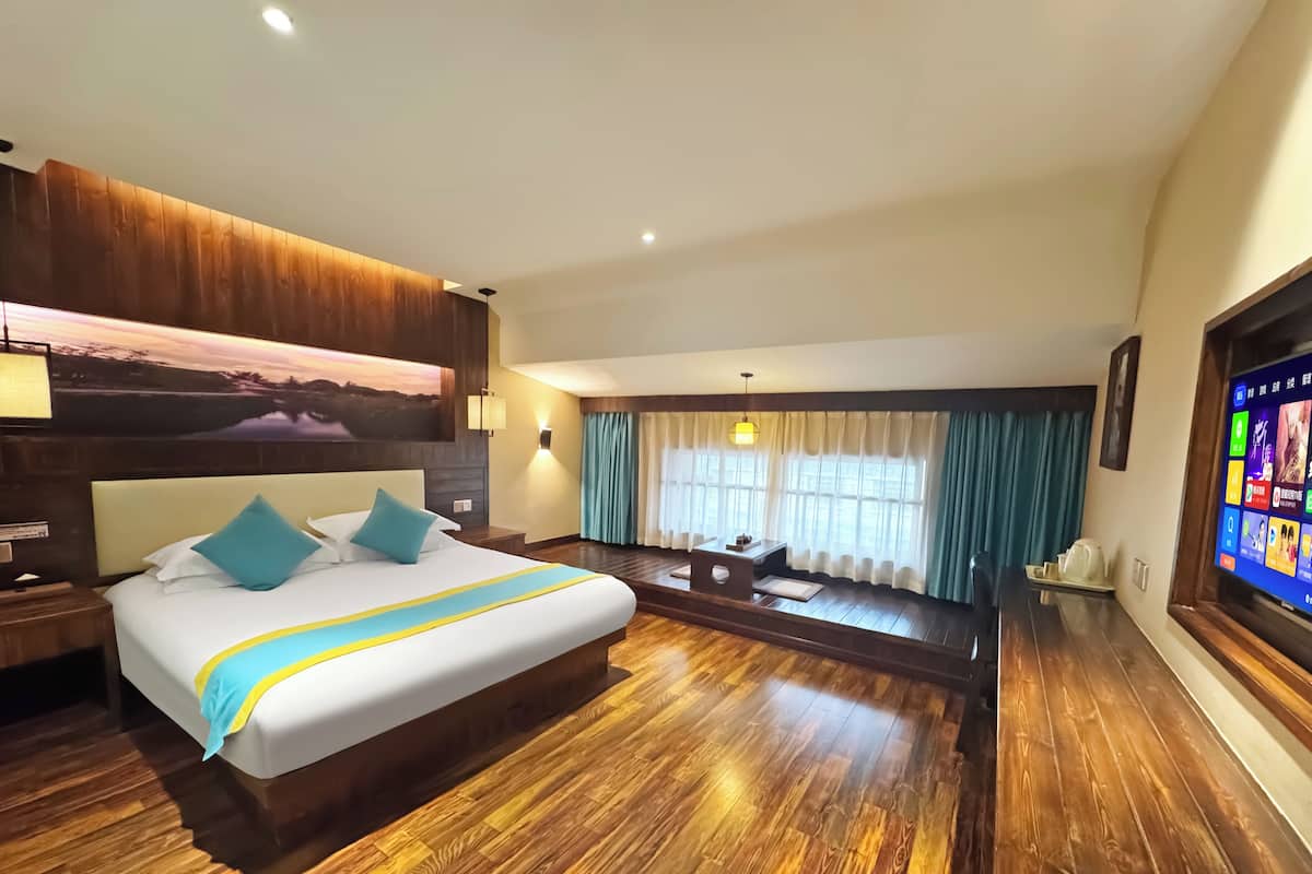 A hotel room with a large bed, wooden flooring, a desk, a TV, and a painting on the wall.