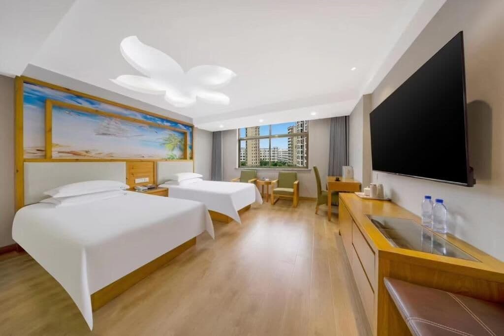 A hotel room with two beds, a desk, a chair, a TV, and a painting on the wall.
