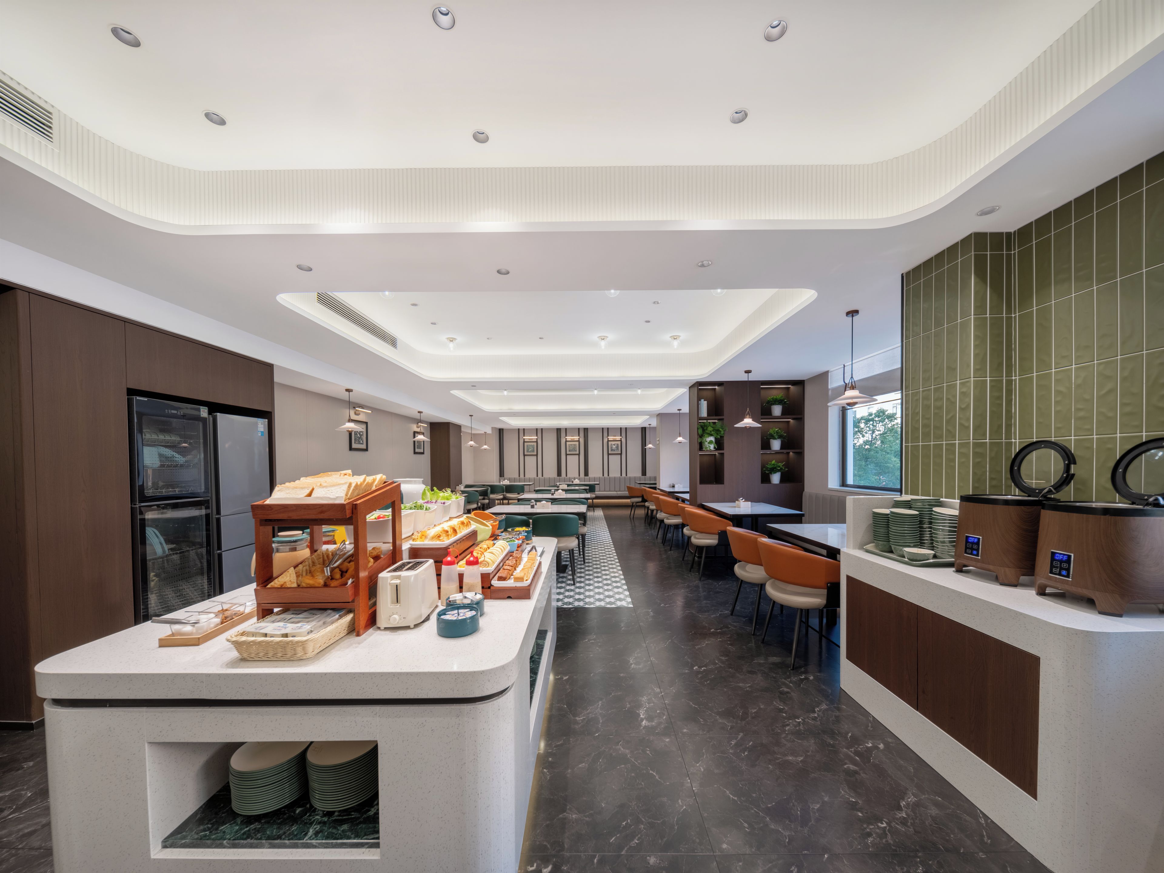 A modern hotel lobby with a central reception desk, seating area, and a buffet setup.