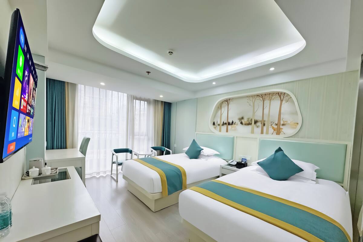 A hotel room with two beds, a desk, a TV, and a window with curtains.