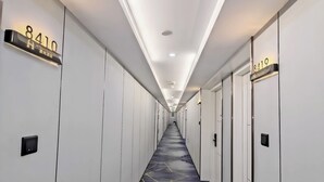 Ein Hotelgang mit nummerierten Türen, einem gemusterten Boden und eingelassener Beleuchtung.