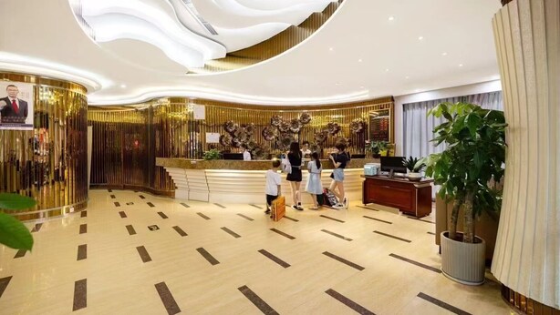 Eine moderne Hotelhalle mit einer Rezeption, einer großen Topfpflanze und einer dekorativen Decke.