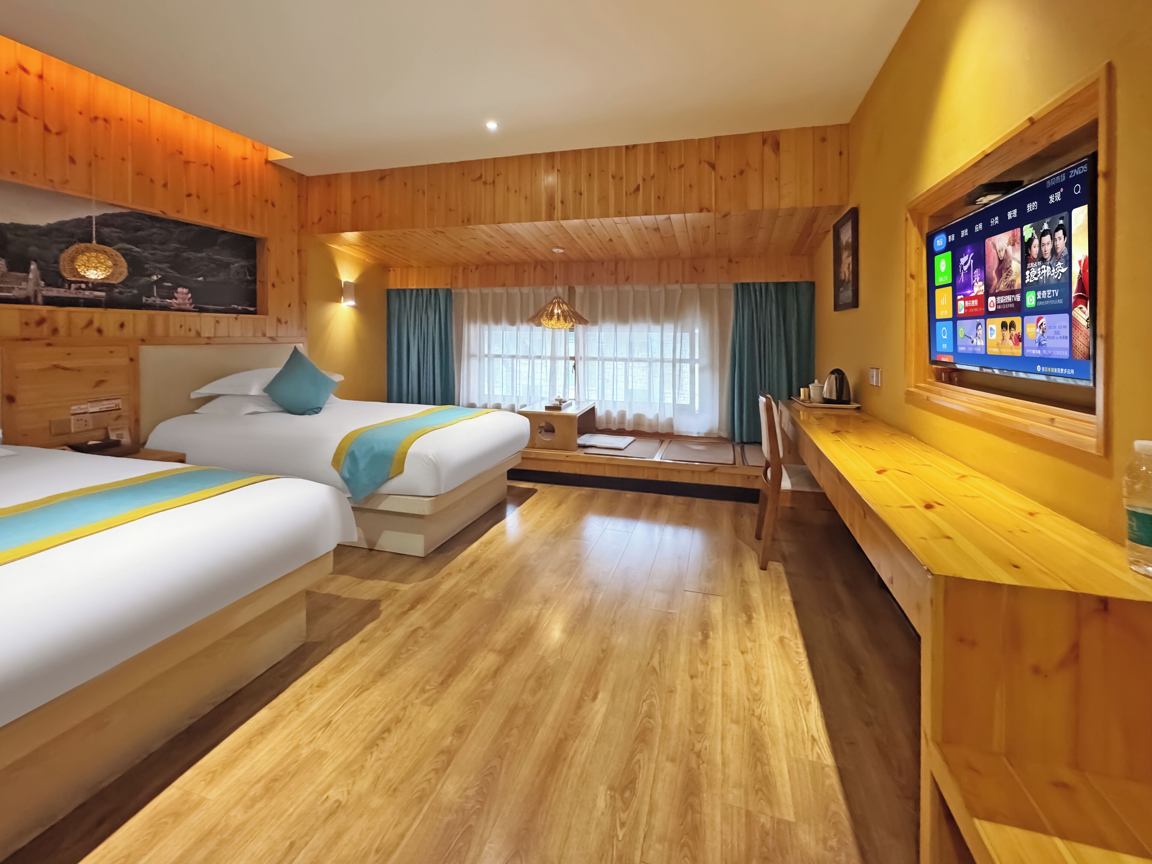 Habitación de hotel con paneles de madera, dos camas con ropa de cama azul y amarilla, un escritorio de madera con televisor y un ventanal con cortinas.