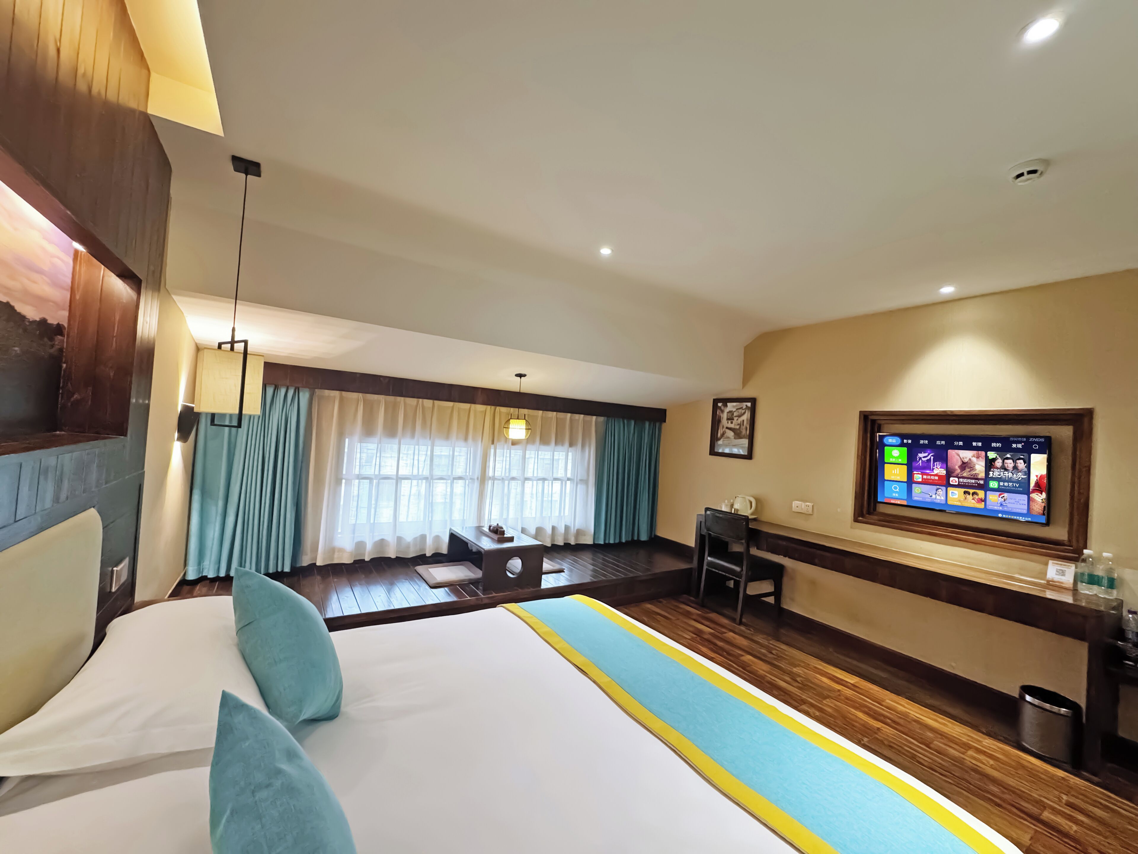 A hotel room with a large bed, a desk, a television, and a window with curtains.