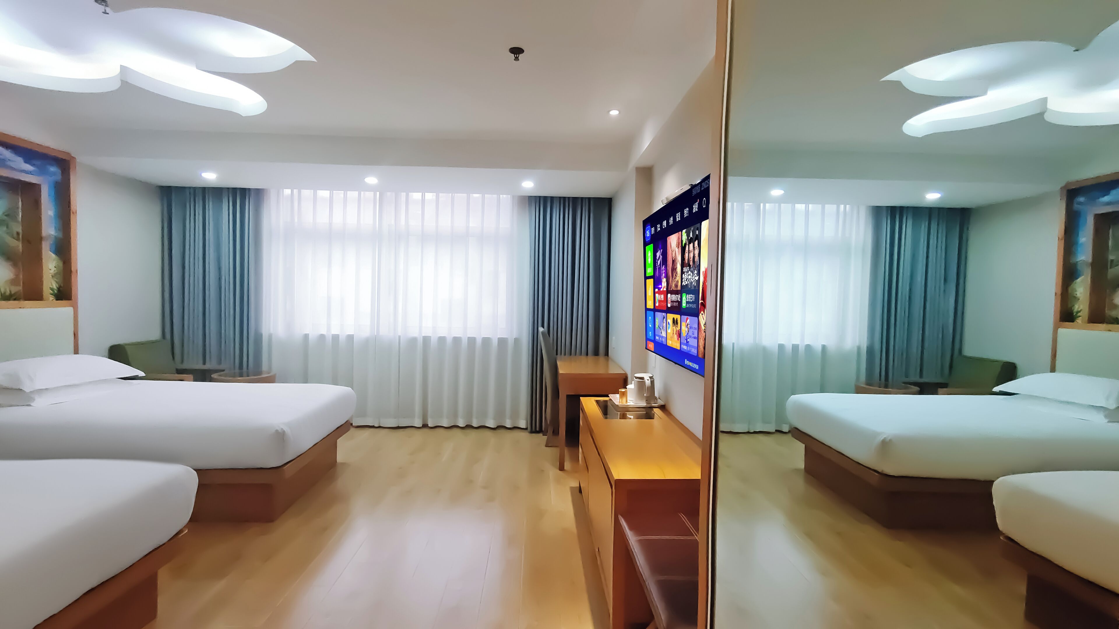 A hotel room with two beds, a desk, a TV, and a large mirror.