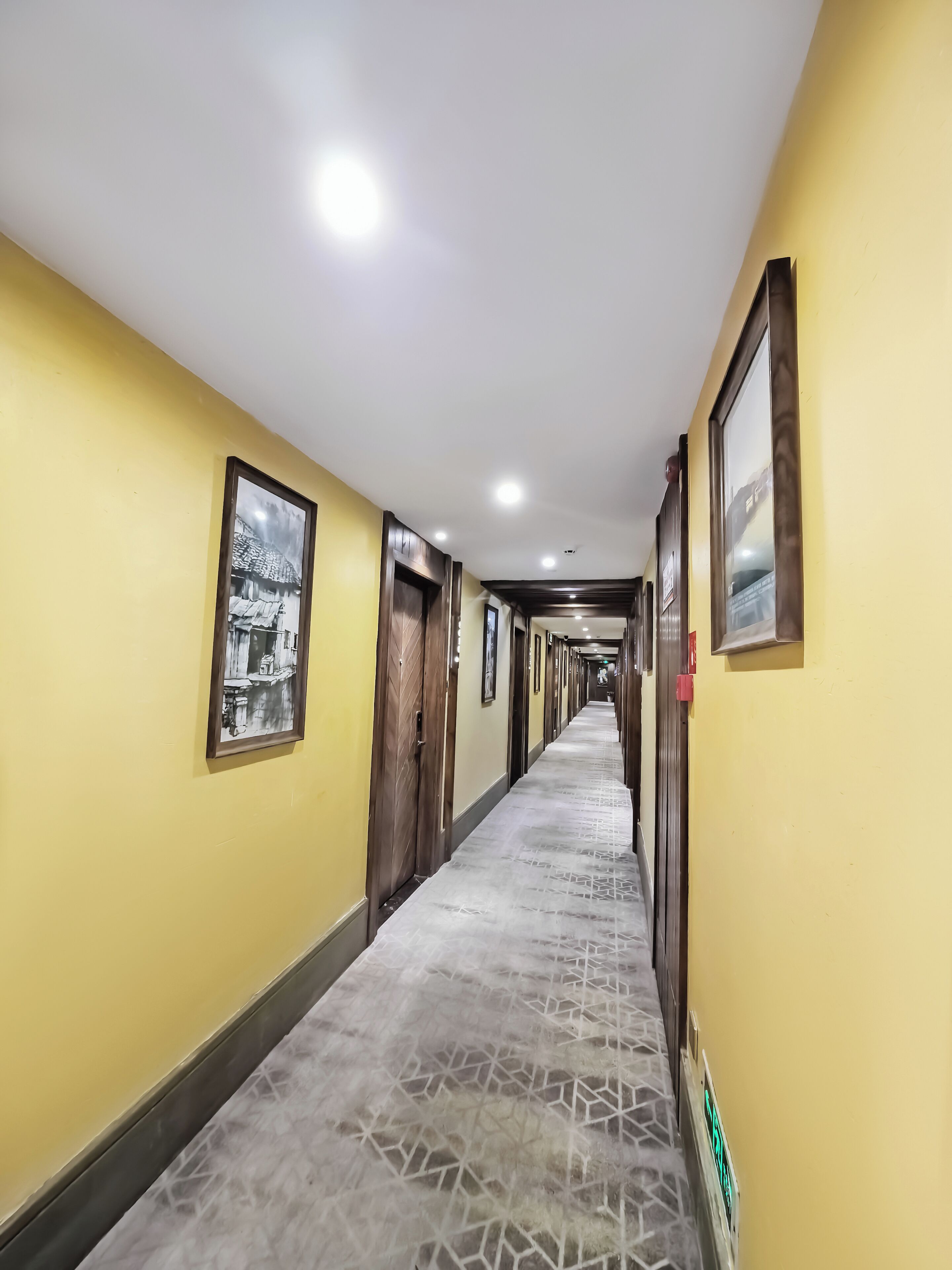 A long hallway with yellow walls, framed pictures, and a patterned carpet.