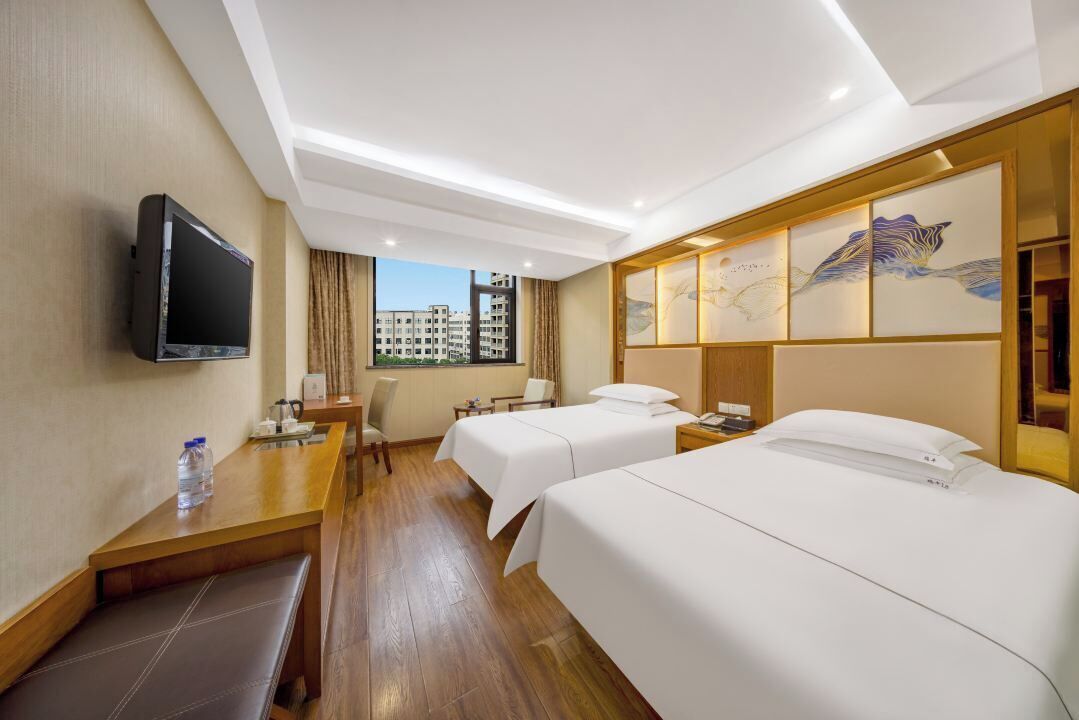 Une chambre d’hôtel avec deux lits, un bureau avec une chaise, une télévision et une grande fenêtre donnant sur la ville.