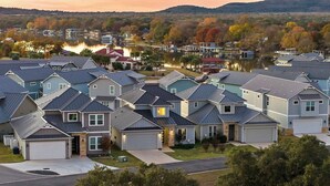 Un quartier résidentiel où les maisons sont dotées de toits à pignons et de garages attenants, le tout étant entouré d’un lac et d’arbres aux feuillages d’automne.