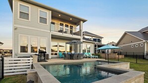 Une maison à deux étages avec une piscine, un espace salon extérieur et un jardin clôturé.