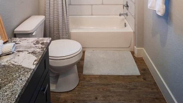 A bathroom with a shower, toilet, and sink, featuring a tiled wall and a painting. - The Sandbar Retreat! (Kingsland)