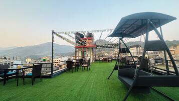 A rooftop terrace with artificial grass, seating, and a view of a cityscape and mountains.