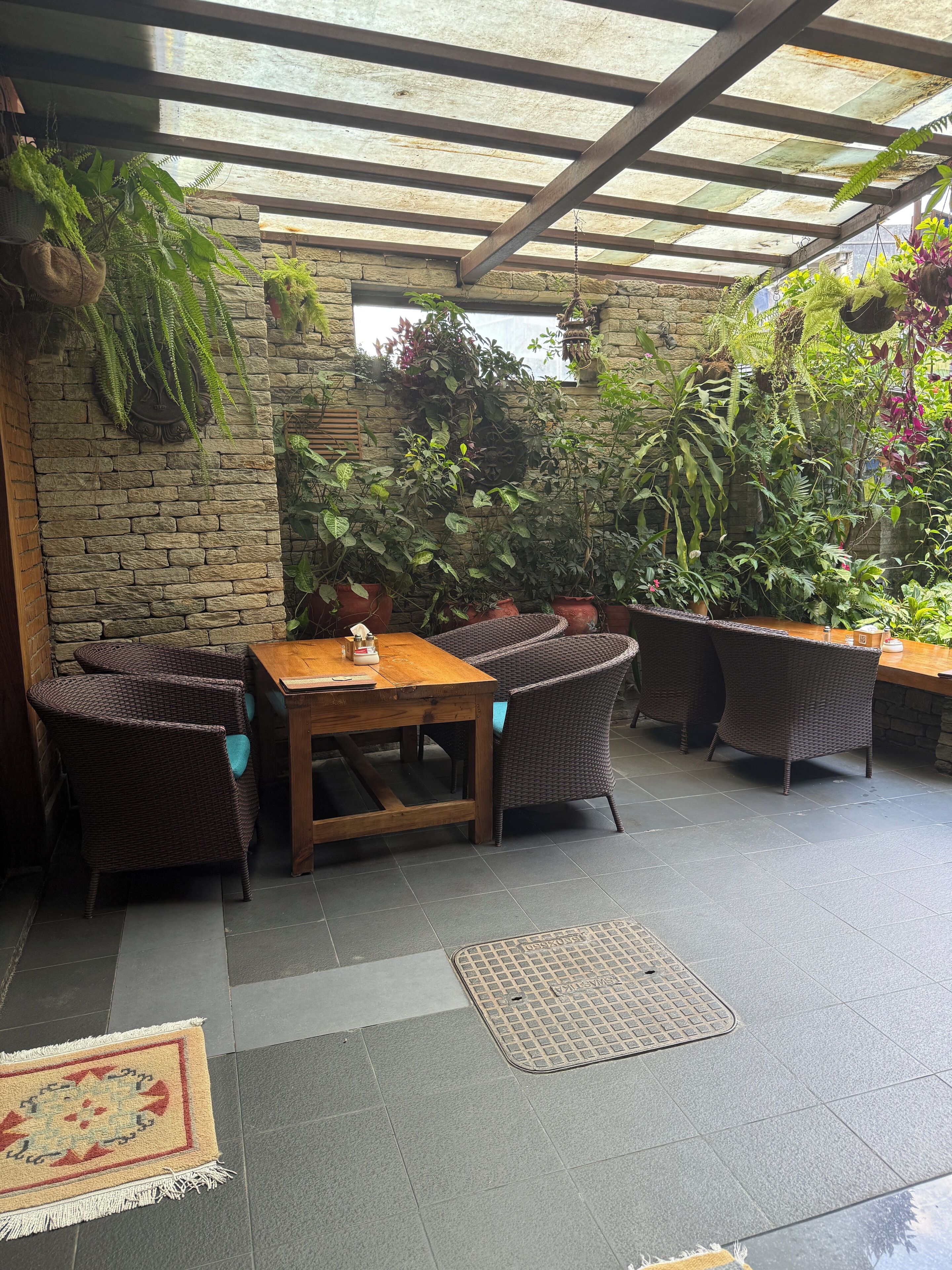 An outdoor patio with wicker furniture, a stone wall, and various potted plants.