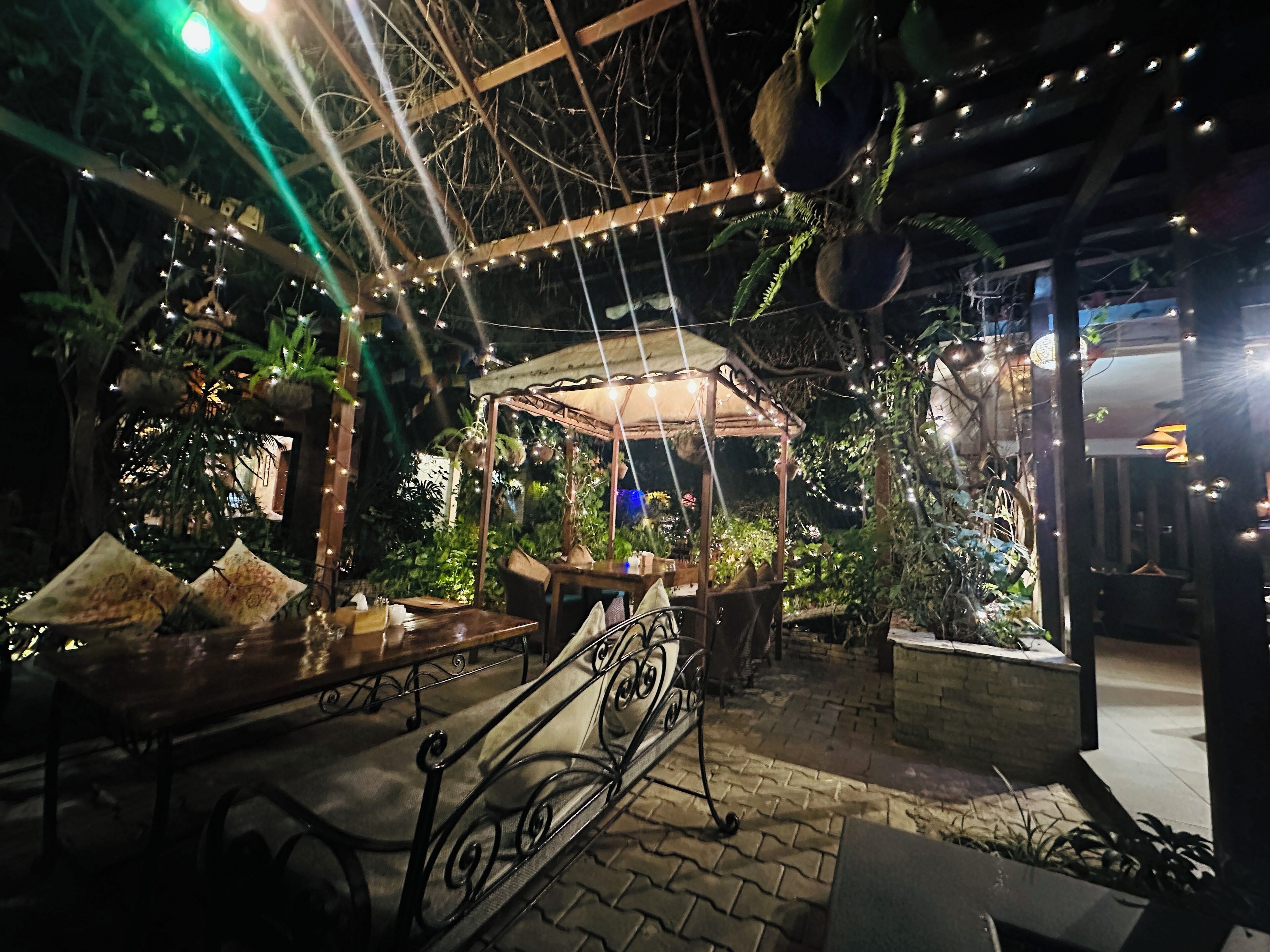 An outdoor seating area with a wooden pergola, string lights, and potted plants.