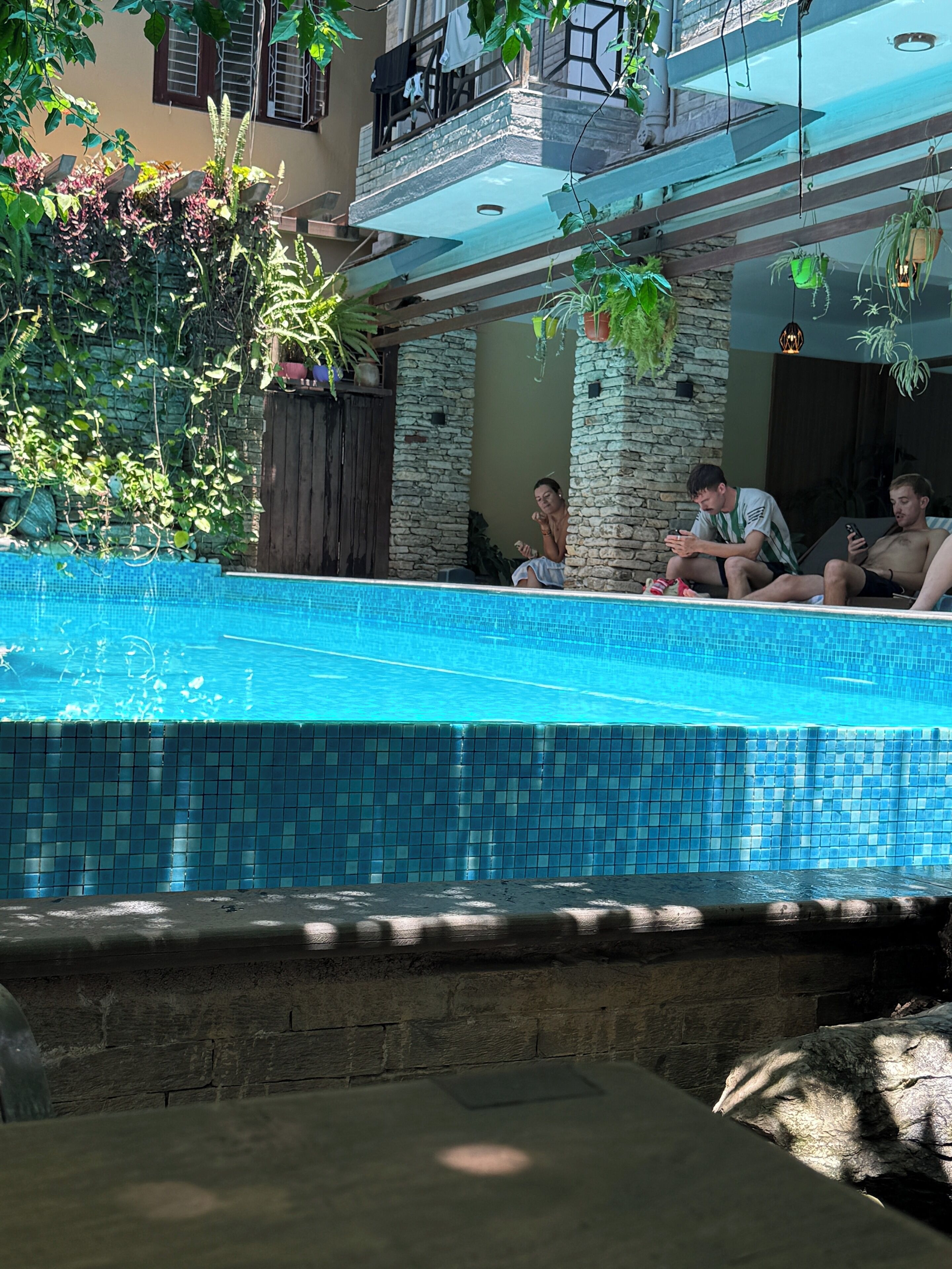 A swimming pool with tiled edges, surrounded by stone walls and potted plants.
