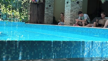 Una piscina con bordes de azulejos, rodeada de muros de piedra y plantas en macetas.